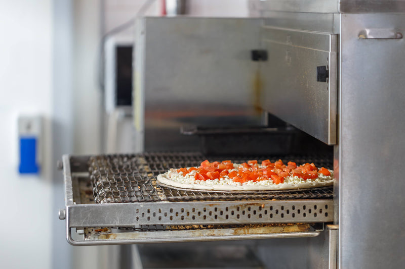 Pizza with red toppings being cooked in a commercial oven.